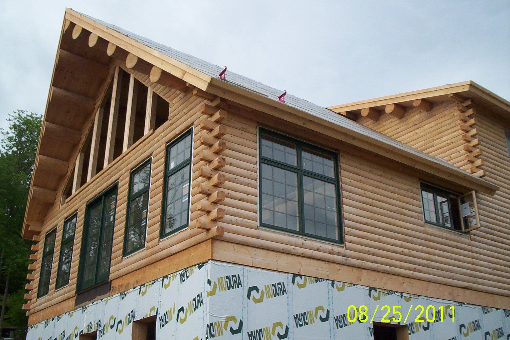 Partially built log-style house exterior with windows and roof framing