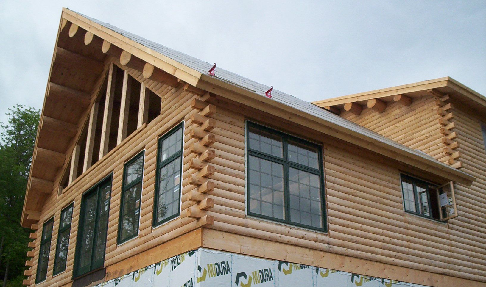 Two-story wooden house with a steep roof, large windows, and exposed timber framing under construction