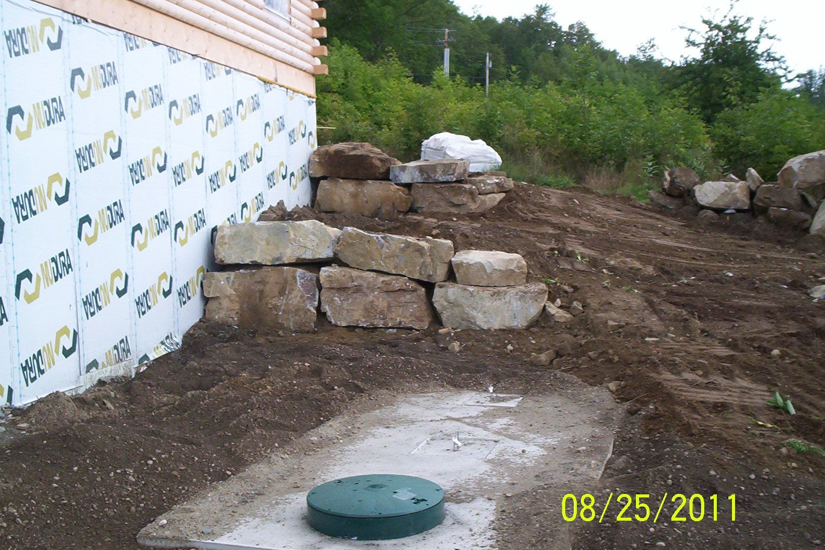 Stone retaining wall and graded dirt beside a house foundation under construction.