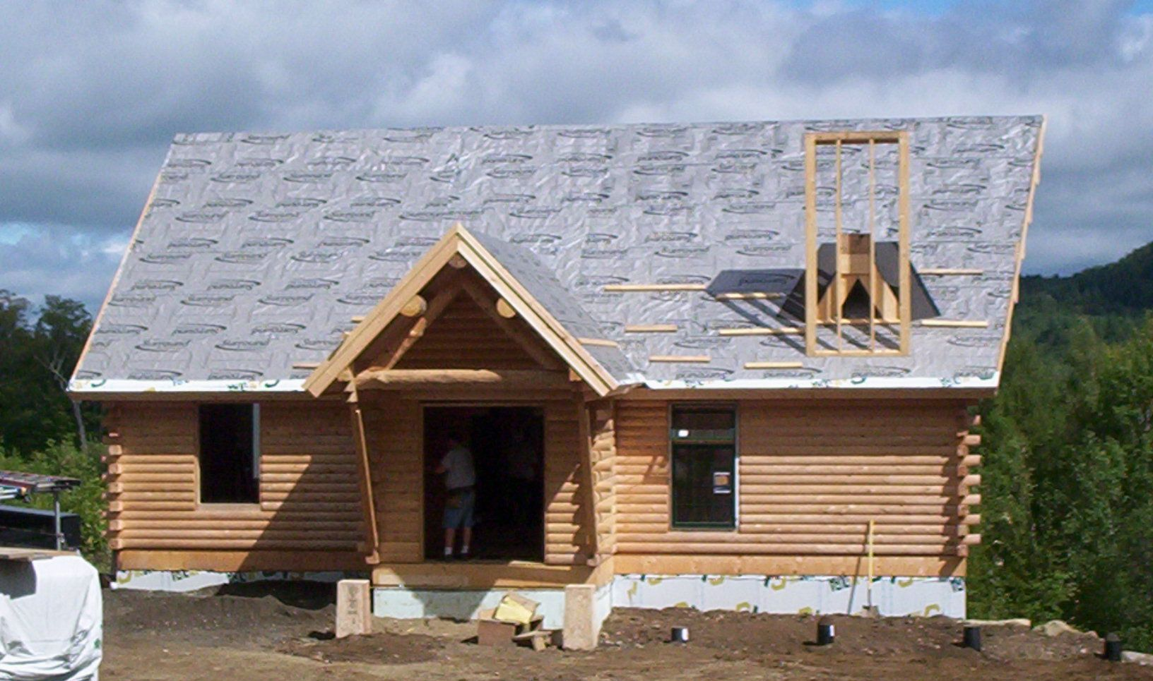 Partially built log cabin with gray roof under construction in a rural clearing