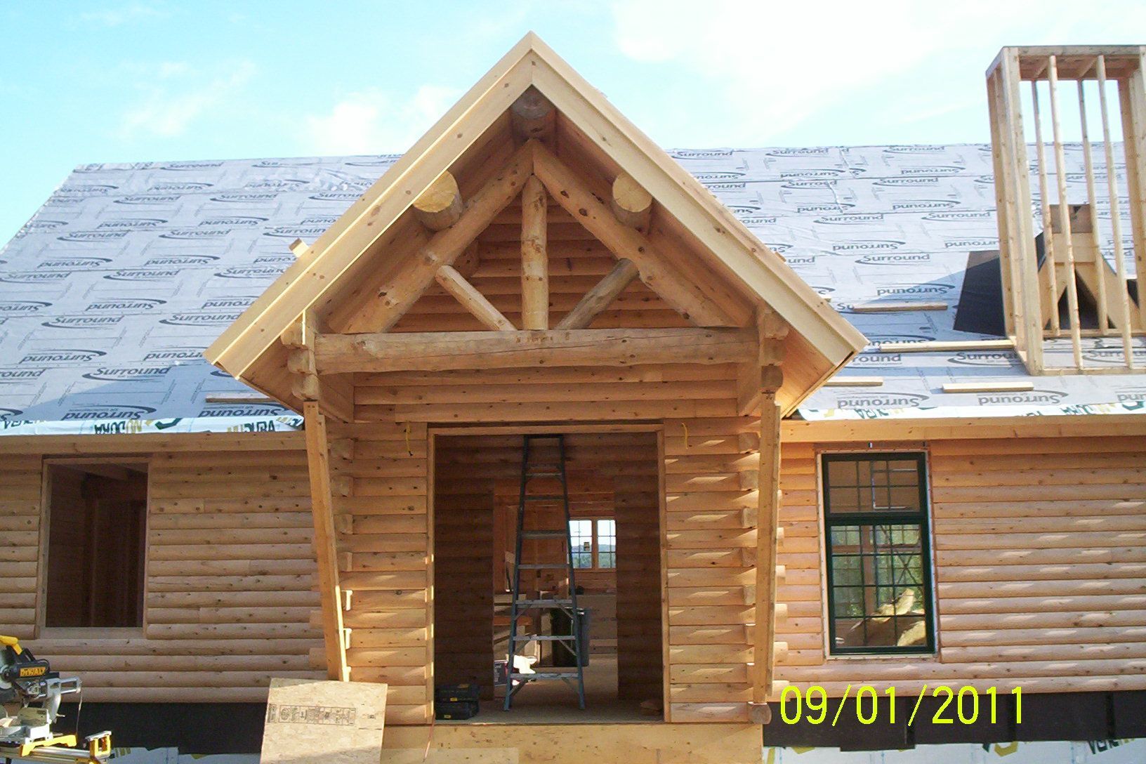 Log cabin under construction with a gabled front entrance and unfinished roof