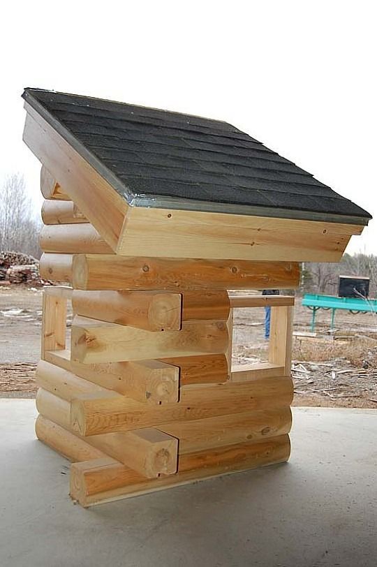Small wooden playhouse with a dark shingled roof outdoors on a concrete surface