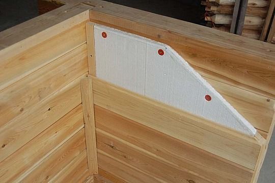 Wooden corner box with a white triangular panel and red fasteners inside a larger wood structure