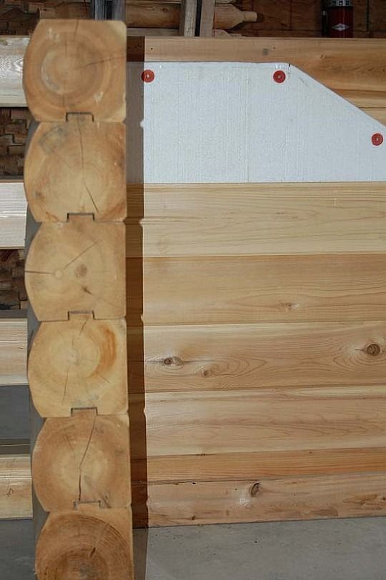 Interior log wall with a light wood door panel and red screws on the left side.