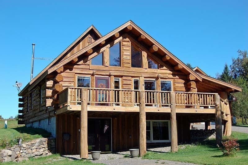 Wooden log cabin with a porch and balcony under a bright blue sky