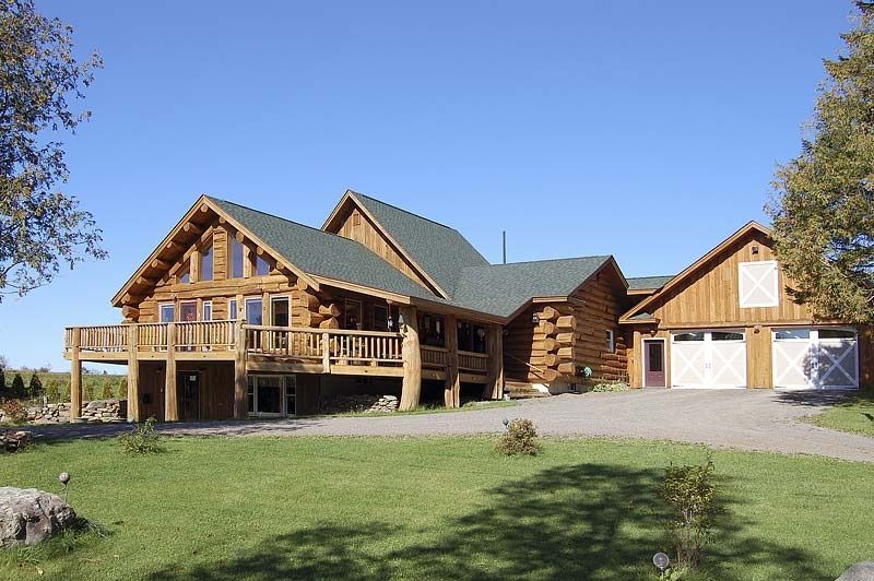 Large log home with green roof and twin garages on a sunny day, set on a grassy property.
