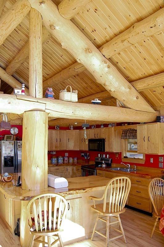 Rustic wooden kitchen with log beams, red countertops, and chairs at a breakfast bar