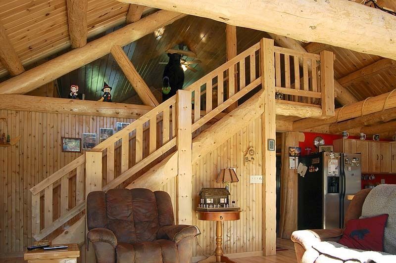 Wooden cabin loft with stairs, balcony, and leather chair in a warm, rustic living room