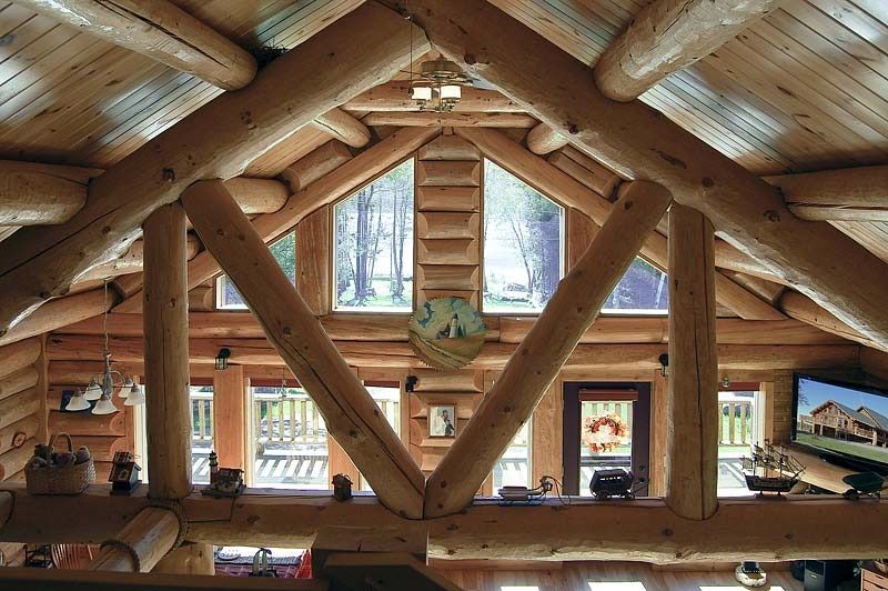 Rustic attic interior with wooden beams, triangular window, and warm natural light