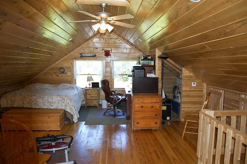 Wood-paneled attic bedroom with a bed, desk, chair, dresser, and window at the far end