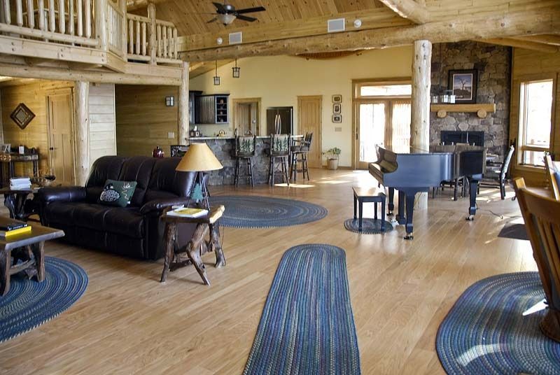 Spacious rustic lodge living room with leather sofas, blue rugs, wood beams, and a grand piano.