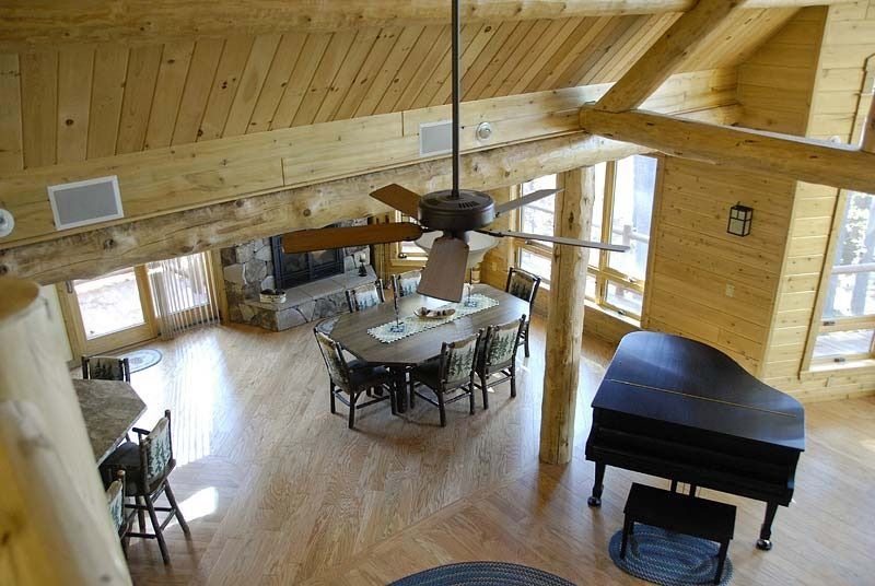 Bright wood-paneled living room with a dining table, chairs, ceiling fan, and grand piano.