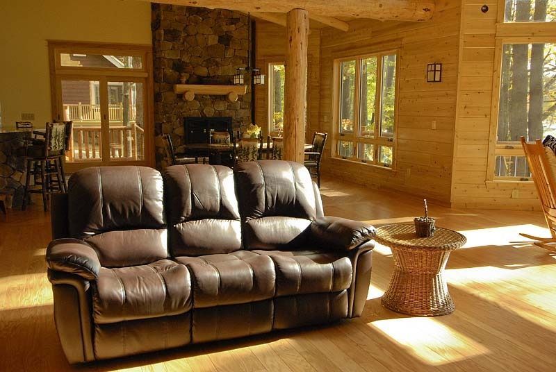 Brown leather sofa in a sunlit wooden living room with a stone fireplace and large windows