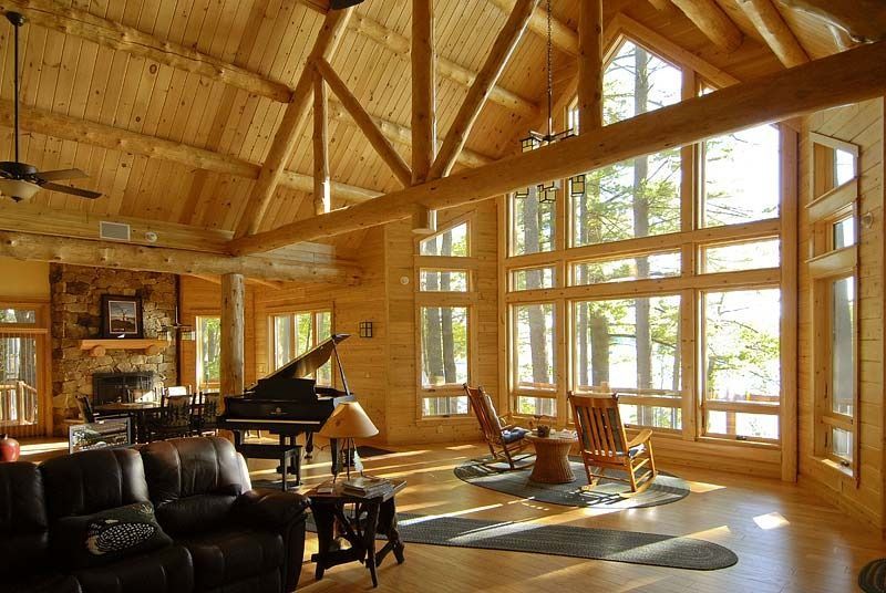 Sunlit wooden cabin living room with a grand piano, black sofa, and large windows