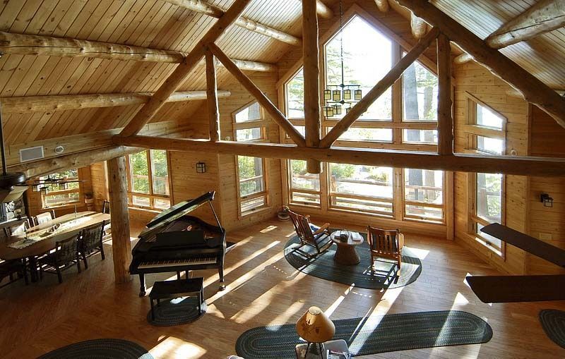 Sunlit wooden loft living room with piano, sofas, and large windows overlooking trees