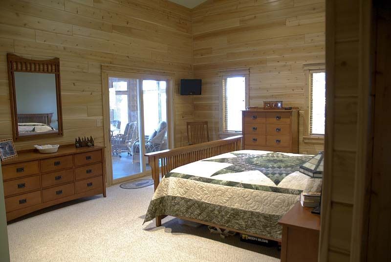 Wood-paneled bedroom with a bed, dresser, mirror, and glass doors leading outside