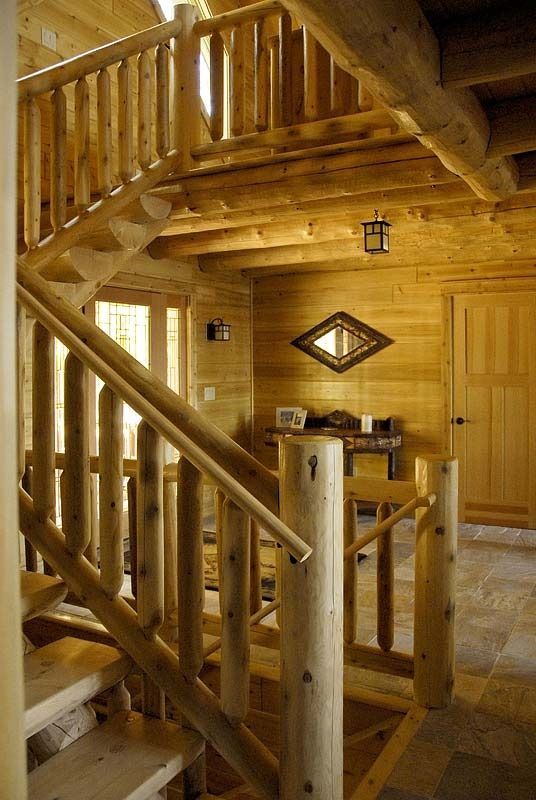 Wooden log cabin interior with staircase, loft railing, and door under warm lighting