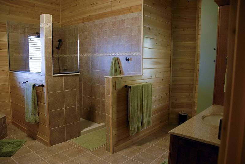 Wood-paneled bathroom with two tiled shower stalls and green towels hanging on the partitions.