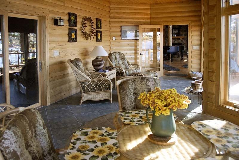 Sunny log cabin porch with wicker chairs, glass doors, and a table with yellow flowers