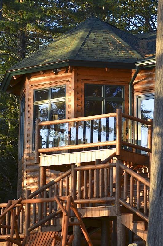 Wooden treehouse with a small balcony and stairs among tall trees.