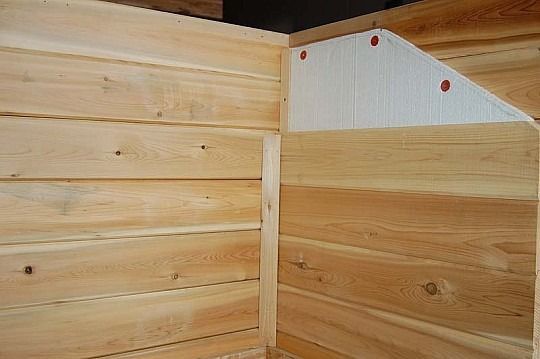 Corner of unfinished wooden walls with horizontal planks and a white triangular panel with red dots.