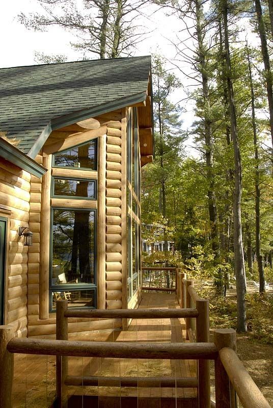 Wooden cabin porch with large windows among tall pine trees in a wooded area