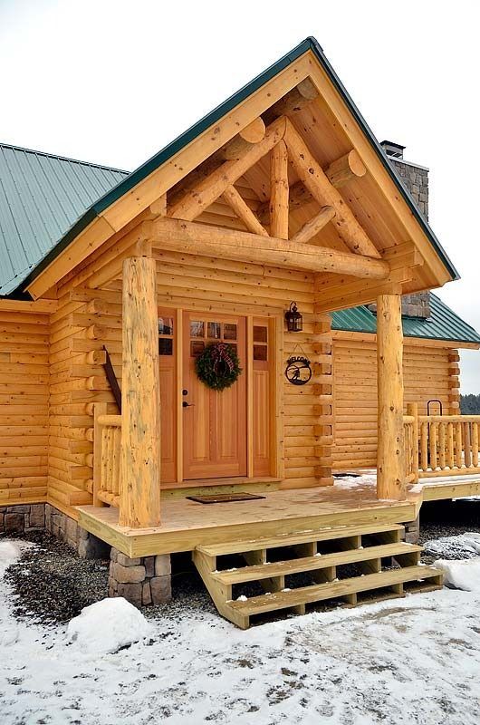 Wooden log cabin with a front porch and steps in a snowy yard