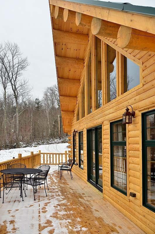 Wooden cabin deck with patio furniture beside snowy woods in winter