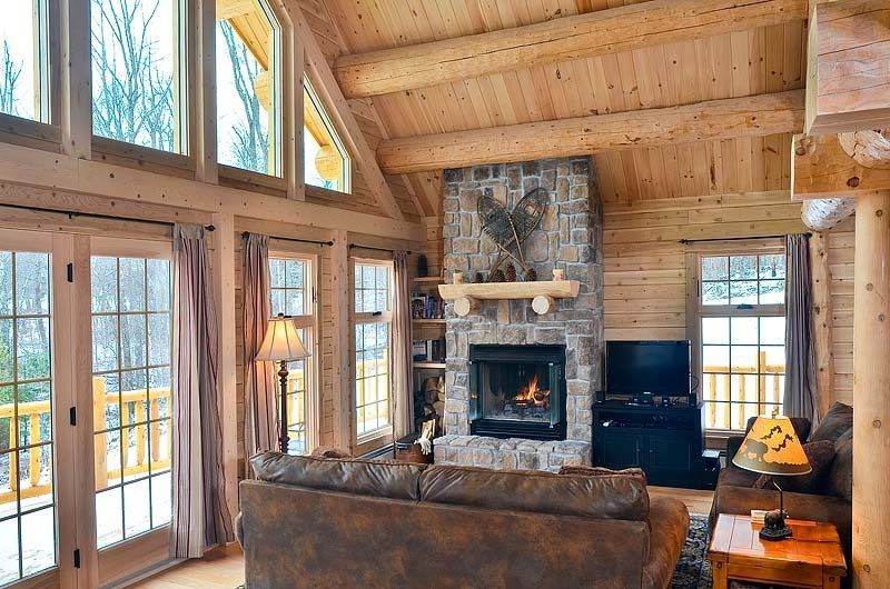 Cozy log cabin living room with stone fireplace, large windows, and mountain views