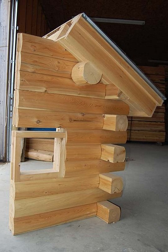 Wooden birdhouse with a slanted roof and small window, shown indoors against a dark background