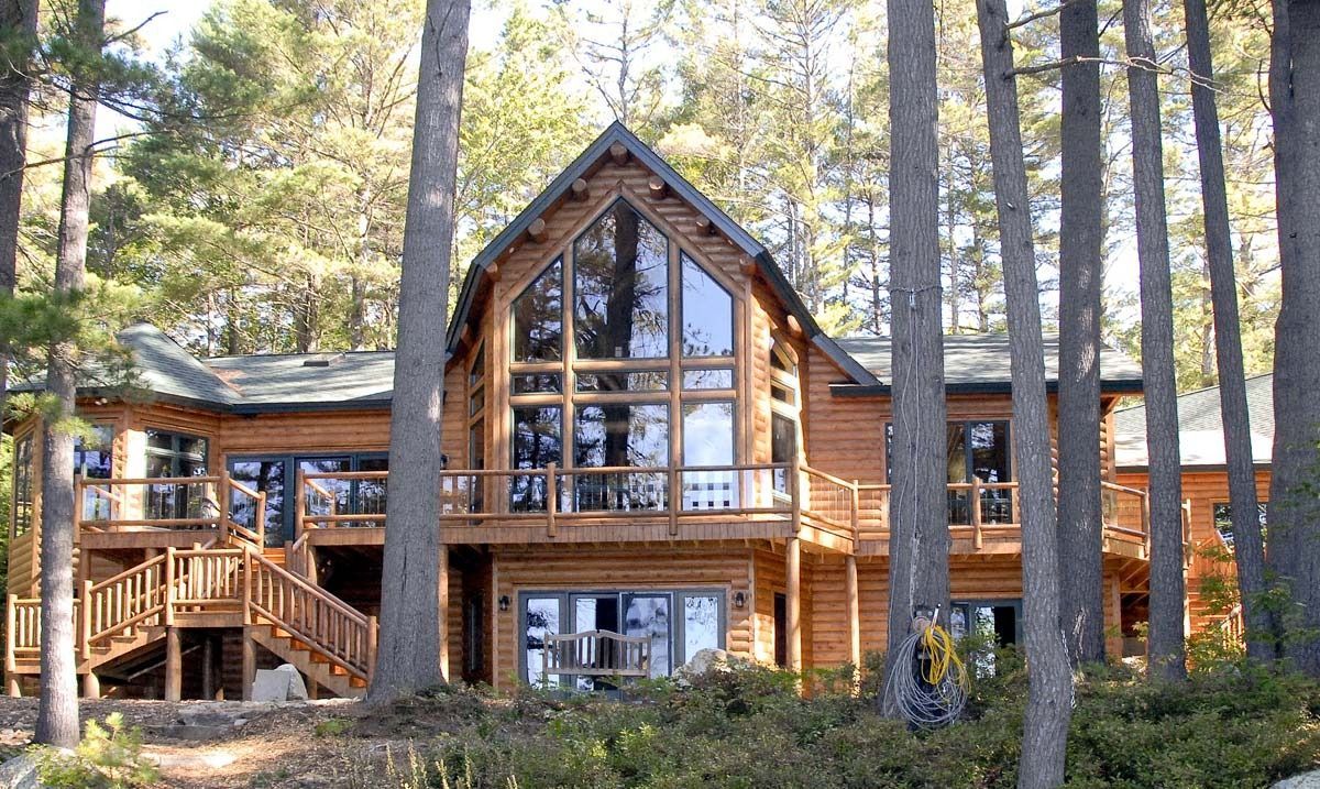 Wooden cabin with large windows nestled among tall pine trees in a forest.