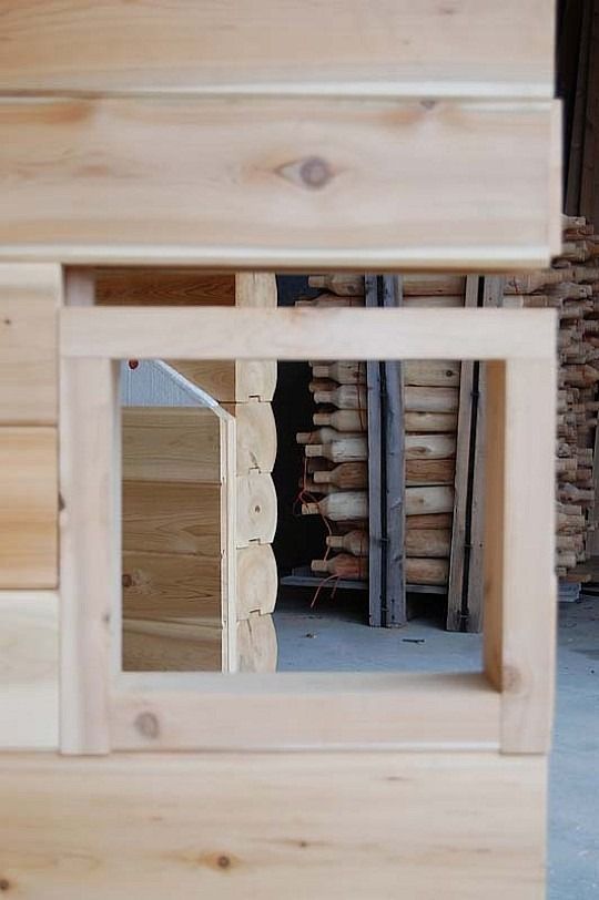 Wooden wall with a square cutout window into a room of stacked bricks and tools