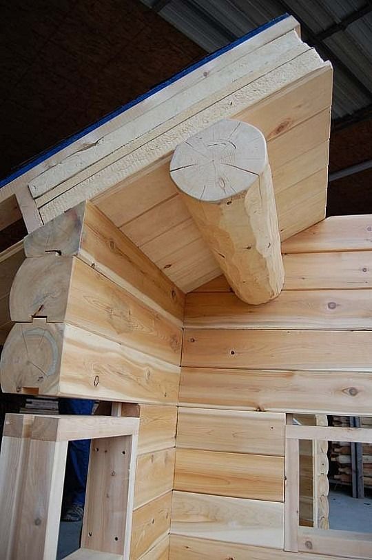 Wooden log cabin corner with exposed roof beam and unfinished interior framing