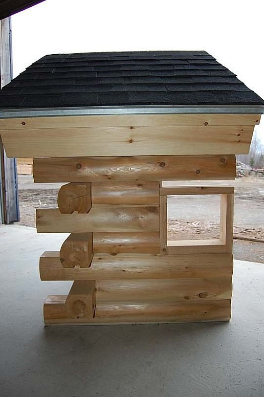 Wooden log-style doghouse with a black shingled roof on a concrete floor
