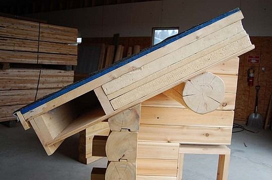 Wooden ramp or chute tilted over a stacked wooden base in a workshop.