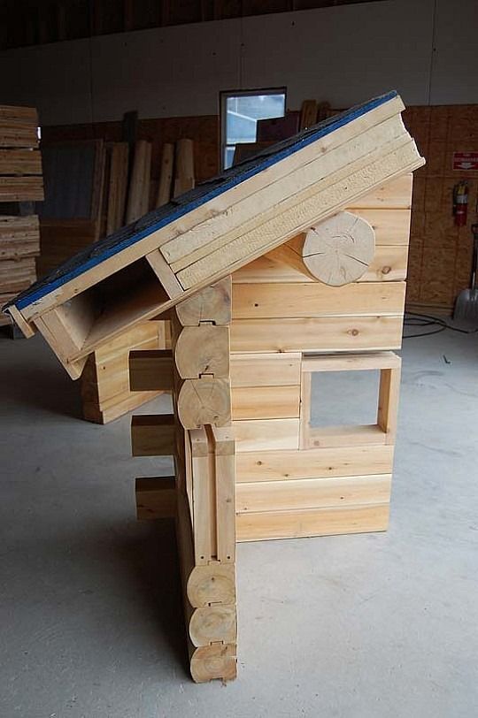 Small wooden doghouse with a slanted roof, viewed from the side in an indoor workshop.