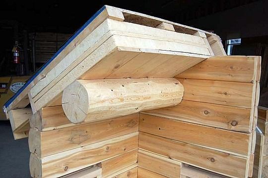 Wooden log cabin corner with a slanted roof and exposed round log support beam