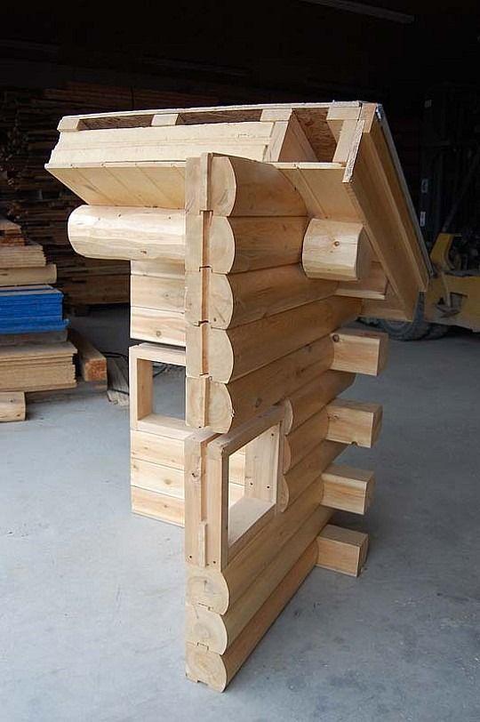 Wooden log cabin wall frame with a slanted roof, unfinished and standing in a workshop.