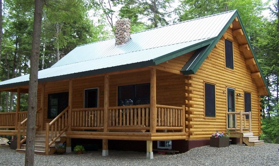 Wooden cabin with a covered porch and green metal roof in a wooded area