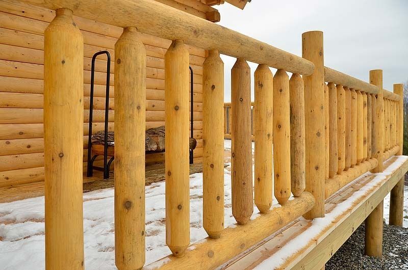 Wooden log porch railing with snow on the ground beside a cabin