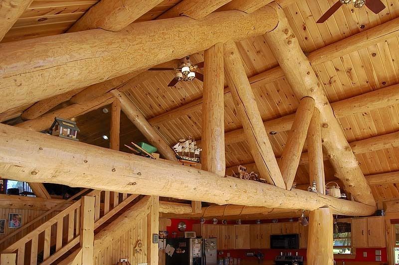 Wooden log-beam interior with a vaulted ceiling and staircase railing below