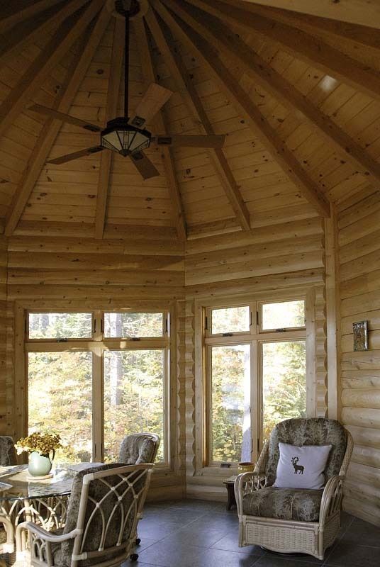 Cozy log cabin sunroom with wood-paneled ceiling, large windows, and wicker chairs