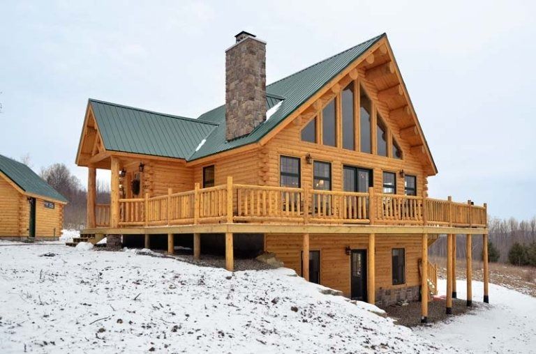 Wooden cabin with green roof and wraparound deck on a snowy hillside