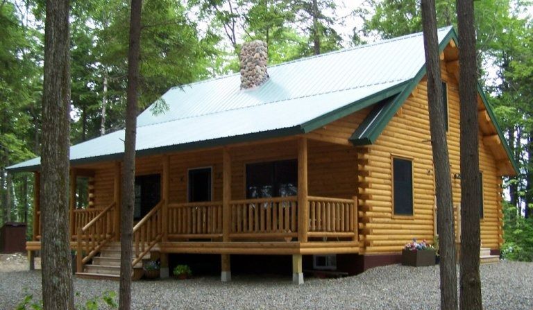 Wooden log cabin with porch and green metal roof in a wooded setting