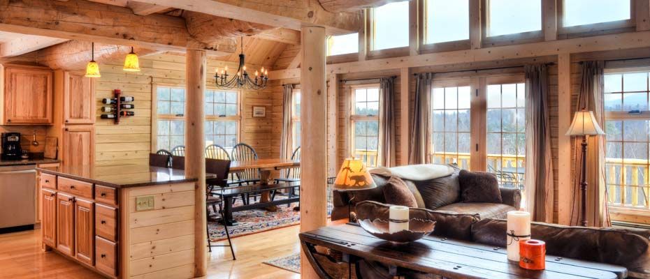 Cozy wooden cabin living room with large windows, sofa, coffee table, and warm natural light