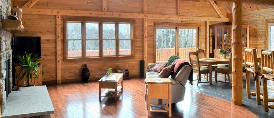 Cozy wooden cabin living room with large windows, sofa, coffee table, and dining area