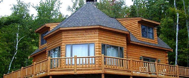 Wooden cabin with wraparound deck and skylights, surrounded by green trees