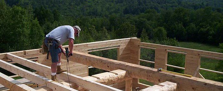 Worker framing a wooden house roof on a construction site with green hills in the background