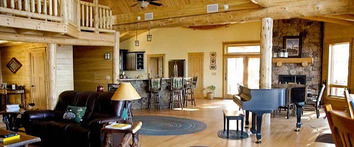 Spacious rustic living room with wood paneling, leather seating, piano, and a dining area in the background