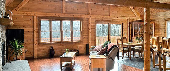Cozy log cabin living room with wood walls, large windows, sofa, coffee table, and dining area